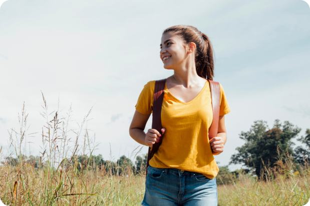 Viajante com sorriso nos lábios em meio à natureza e com sua mochila nas costas